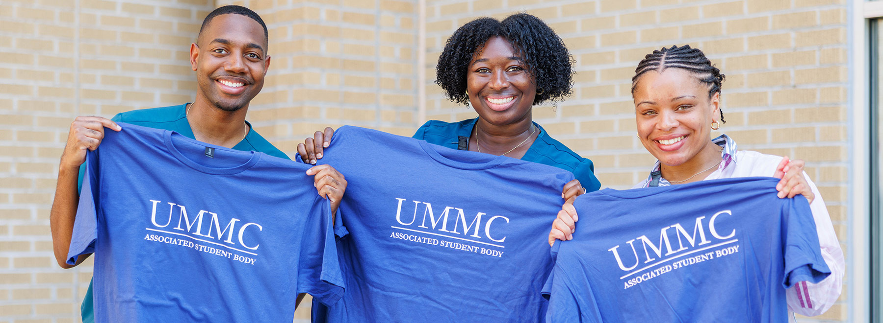Three people holding up blue UMMC Associated Student Body T-shirts.